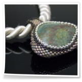 Grüner Stein umperlt mit Rocailles an einer Satinkordel