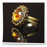 Bernsteinfarbener Glascabochon, umperlt mit Rocailles.